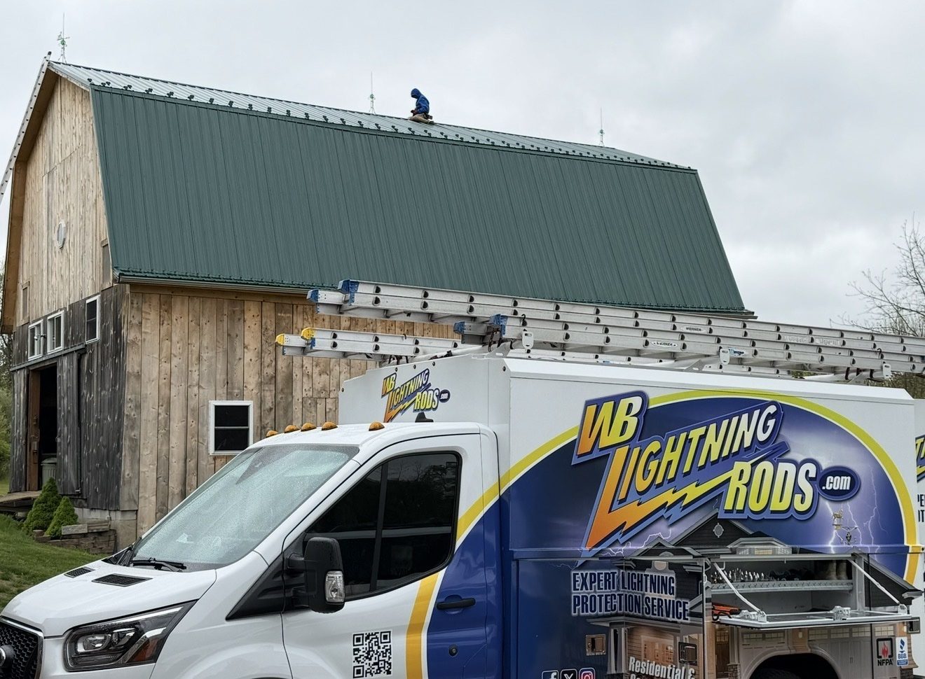 WB Lightning Rods van in front of a gambrel-roof dairy barn while a crew member installs lightning rods on the ridge