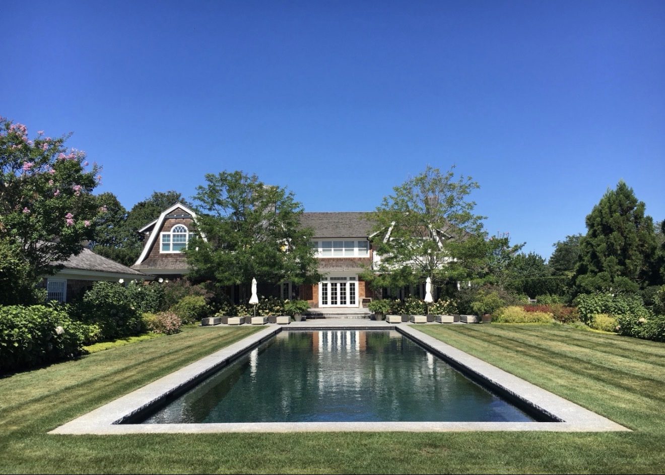 Shingle-style Hamptons estate home with manicured lawns and a long reflecting pool